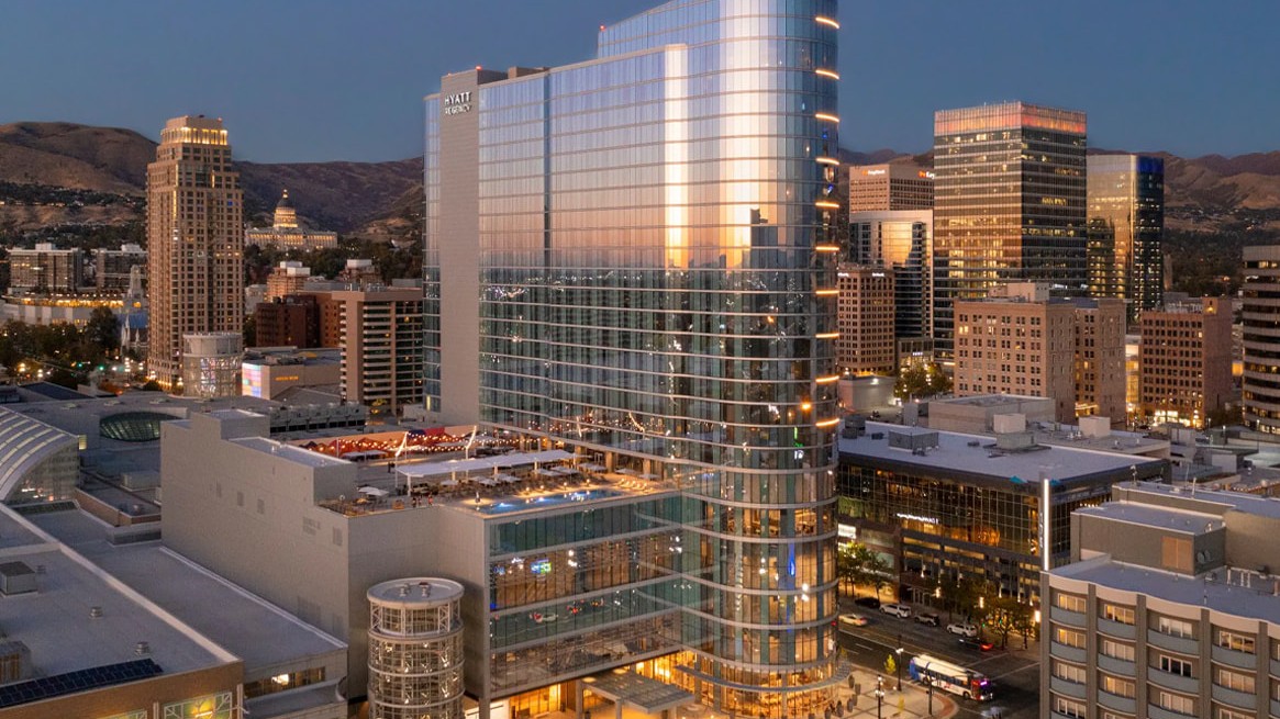 A modern glass skyscraper downtown at dusk, with surrounding buildings and distant mountains.