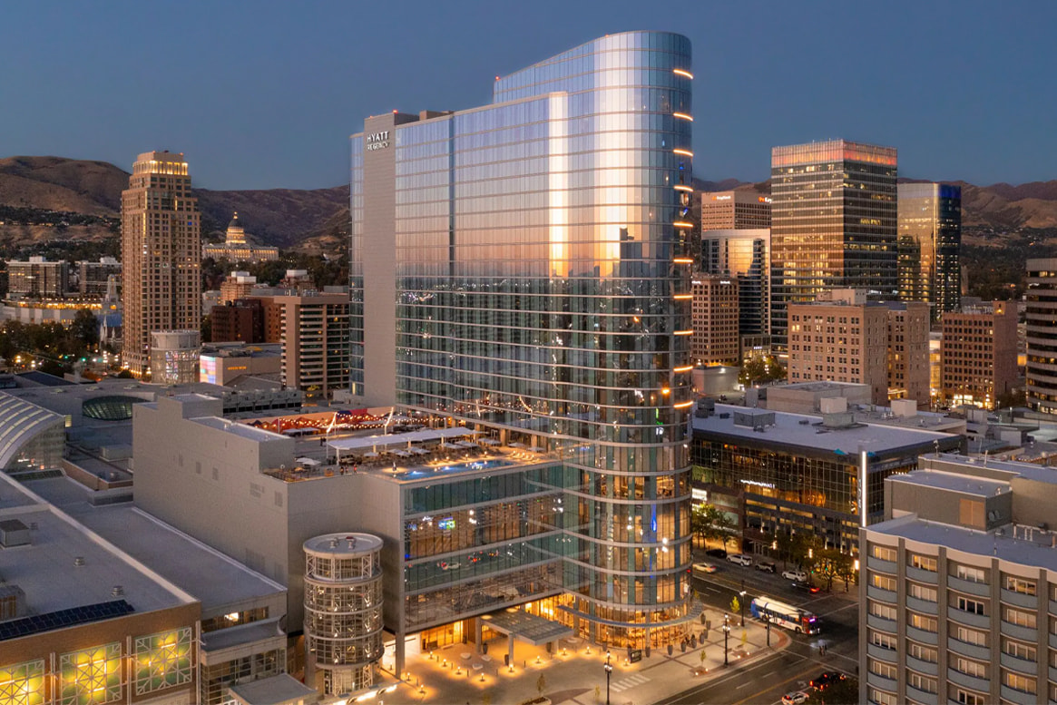 A modern glass skyscraper downtown at dusk, with surrounding buildings and distant mountains.